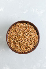 Organic dry buckwheat groats in a brown bowl on a gray background. Vegetarian and vegan food. Concept of healthy eating. Vertical orientation. Top view.