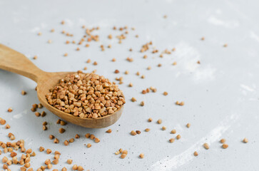 Organic dry buckwheat groats in a wooden spoon on a gray background. Vegetarian and vegan food. Concept of healthy eating. Horizontal orientation. Selective focus. Copy space.