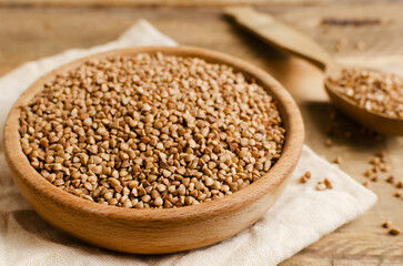 Organic buckwheat groats in a wooden bowl with spoon on a linen napkin on a wooden table. Rural style. Concept of healthy eating. Horizontal orientation. Selective focus