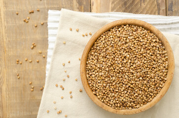 Organic buckwheat groats in a wooden bowl on a linen napkin on a wooden table. Rural style. Concept of healthy eating. Horizontal orientation. Top view. Copy space