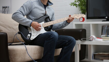 Male hands at home play and tune the electric guitar is engaged in music realizes listening...
