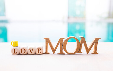 Mom wooden font with love wooden cube and coffee cup on swimming pool edge, mother's day card...
