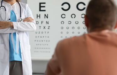 Focus on female ophthalmologist standing in clinic office and performing health examination to male...