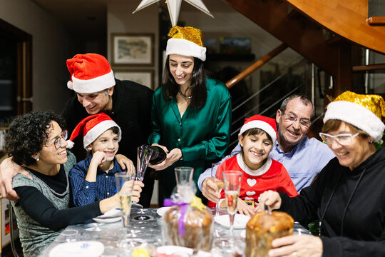 Three multigenerational family celebrating christmas dinner together at home. Spanish happy children in santa hats, parents, and grandparents enjoying xmas celebration together.
