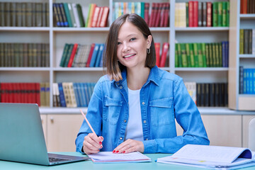 Young female university student looking at camera with laptop in library