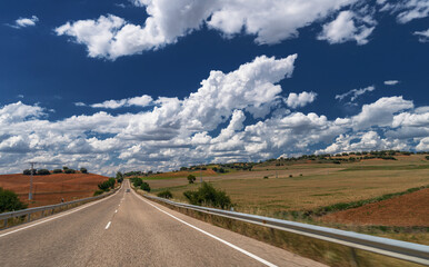 Country road stretching to the skyline between hills and fields and stunning skyscape over it.