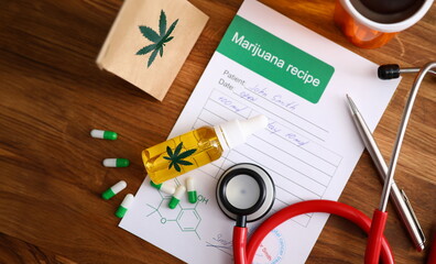 Top view of paper marijuana recipe. Colourful pills and cannabinoid oil lying on wooden desk. Red...