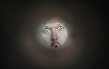 Focus on facial expression of person. Young guy with blue eyes looking through thin tube. Cheerful character with mustache and open mouth. Humorous person