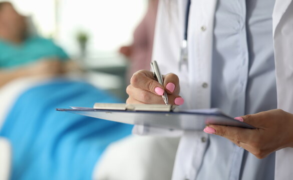 Focus On Female Hand Holding Paper Folder And Writing In Important Documents By Pen. Female Doctor Asking Well-being Of Patient. Healthcare And Medicine Concept