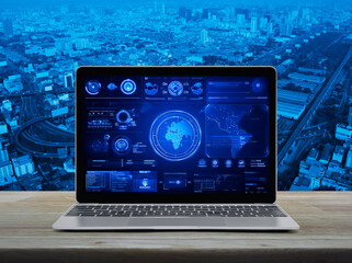 Laptop computer with digital world map with data charts and stats screen on wooden table over city tower, street, expressway and skyscraper, Futuristic user interface technology online concept