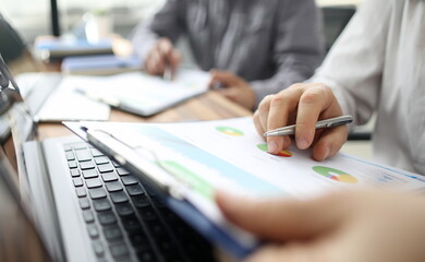 Close-up of clipboard with pie diagrams and information on project results. Man with laptop making report or planning new business activity. Statistics analysis at work