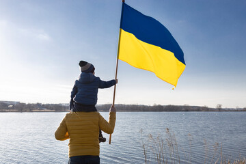 boy sitting on the shoulders of a man, dad with son, with a large flag of Ukraine outdoors. Patriotic education. Pride, national freedom, faith in victory. Stop the war. day of dignity and freedom