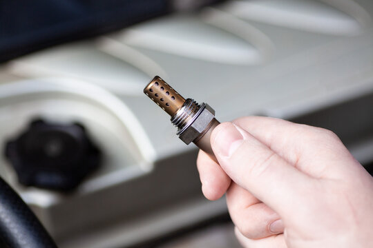 Oxygen sensor for gasoline and diesel engines in the hand against car engine. Mechanic holds oxygen sensor. lambda probe