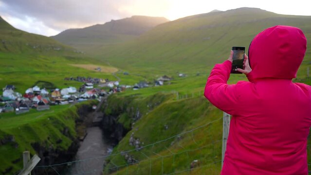 Female tourist taking sunset photos of Gjov in Faroe Islands for social media