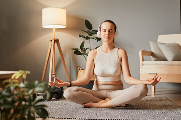 Caucasian woman wearing headphones while practice yoga meditation exercise at home sitting on floor...