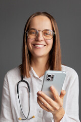 Online doctor's office. Digital health specialist. Mobile phone prescription. Video call with a physician. Cheerful woman doctor wearing white medical lab coat stethoscope and glasses using cell phone