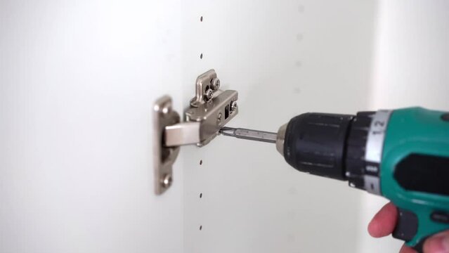 Cabinet hinge installation. Screwing screw with screwdriver on wooden furniture.