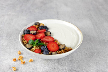 Yogurt bowl with granola and fresh berries: strawberries and blueberries on a gray background. 