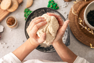 Hands knead dough on a table, decorated with festive decorations for Christmas.
