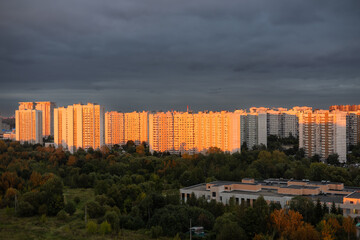 Fototapeta na wymiar Tall multi-storey buildings in the rays of the setting sun. A beautiful residential area of the city at sunset against a cloudy sky. Multi-storey residential buildings in an urban area at sunset.