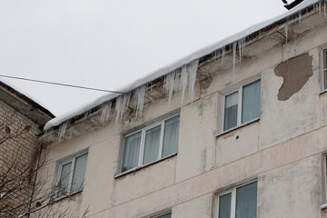 Fototapeta na wymiar Icicles hanging from the roof of the house. Picture of winter snowy Magadan city, Russia.