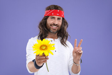 Stylish hippie man with sunflower showing V-sign on violet background