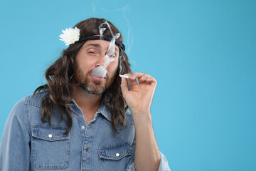 Stylish hippie man smoking cigarette on light blue background, space for text