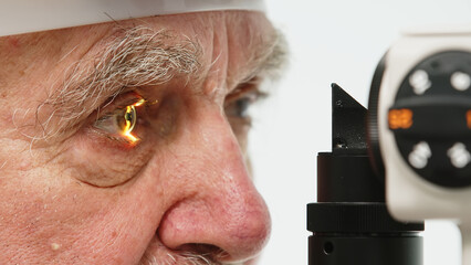 An elderly man in a clinic with an ophthalmologist examines his eyes with a slit lamp and checks...