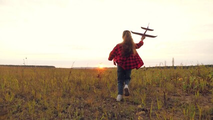 Girl runs across grass field with toy airplane in hand heading toward sunset