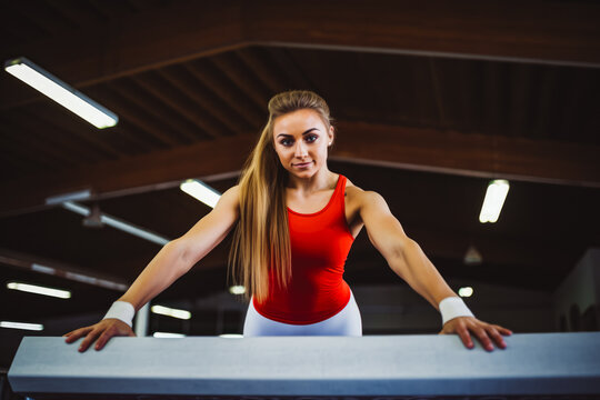 Beautiful female athlete doing a very complicated trick on gymnastics balance beam, athletic woman looking focused while preparing for performance