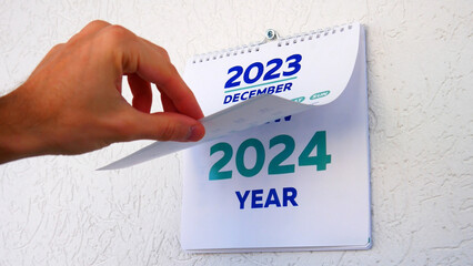 Close-up of a male hand flipping through the December page of 2023 wall calendar followed by the...