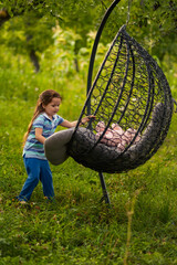 A girl puts things in order on a hanging chair that stands in nature