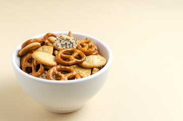 A mix of snacks in a white bowl on a light background. Pretzels with salt, crackers of various shapes and with seeds. Fast food. Harmful snack. Horizontal orientation. Copy space