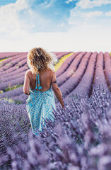 Travel wanderlust lifestyle people concept. Back view portrait of woman walking in lavender field wearing blue trendy boho dress. Blue sky in background. Concept of vacation in scenic destination.