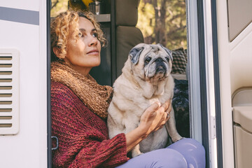 One woman sitting on the camper van door with old nice pug dog looking outside and enjoying relax...