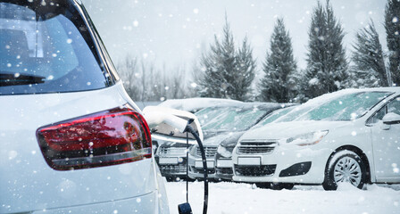 Close up of electric car with a connected charging cable on the blurred background of a snow covered parked cars. - Powered by Adobe