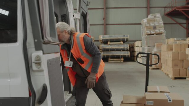 Medium long shot of male storage worker loading packages into cargo van and preparing for shipping to clients