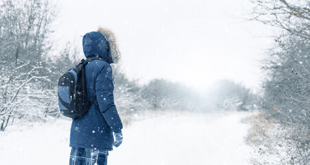 Back view of traveler in a blue jacket with a fur hood and a backpack on the background of a winter...