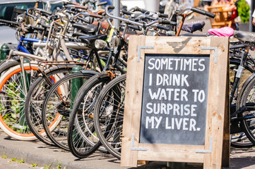 Sign beside some parked bicycles saying "Sometimes I drink water to surprise my liver",