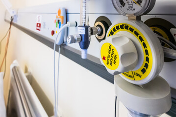 Bed head unit in a hospital ward showing a suction vacuum pressure gauge, an oxygen supply and a nurses call bell.