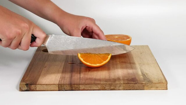 A hand expertly slices an orange into smaller pieces using a knife and cutting board.