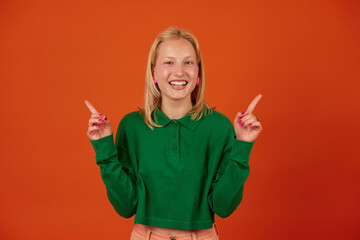 Beautiful young woman raising index fingers in eureka gesture on orange background