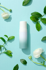 Top view of a cosmetic bottle placed in the center of the frame, surrounded by fresh green tea leaves and white flowers. Mockup for natural cosmetics advertising.