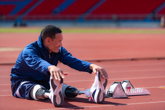 Disabled athletic man stretching and warming up before running on stadium track
