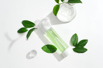 Green tea extract toner bottle on a background of leaves and glass props. Homemade cosmetics,...