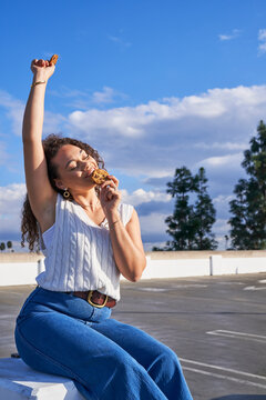 Woman eating cookie outdoors hand in air taking bite