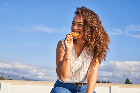 Woman eating cookie outdoors taking a bite smiling