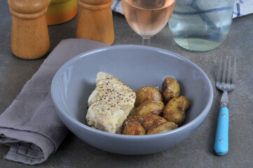 Dos de cabillaud sauce moutarde avec des pommes de terre servis dans une assiette avec une fourchette et un verre de vin
