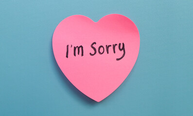 The word sorry written on a pink sticky note in the shape of a heart isolated on a blue background....