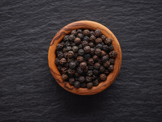 black pepper seeds in wooden bowl on the surface of a black stone